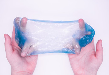 Fototapeta premium Close up of game with light blue slime in someone's hands on a white background. The mucus is crushed, stretched, torn and squeezed by hands