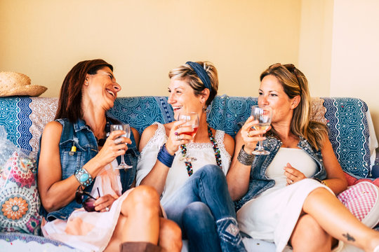 Three Friends Women Laugh And Have Fun Sit Down On A Sofa - People In Friendship At Home - Trendy Young Ladies - Caucasian Trendy Adult Females Drinking Red Wines Together