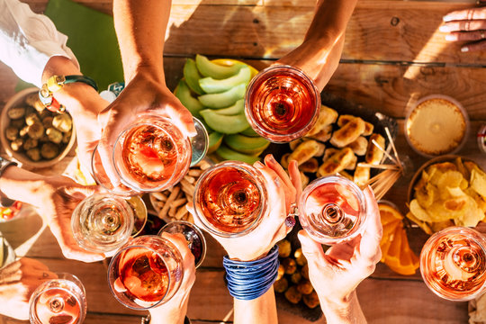Group of happy people toasting  together with cups of red wine under the sun light in a sunny day - outdoor leisure activity for women having fun with drinks - wine and winery concept