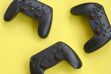 Three modern black gamepads on yellow background. Lets play video games together with friends concept. Cooperative teamplay © mehaniq41