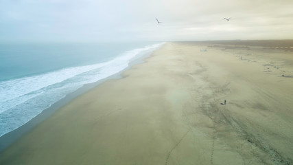 Long beach in the french coast. In the picture we can see two seagulls flying and a man in the middle if the beach on a foggy morning. 