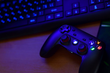 Modern gamepad lies with keyboard on table in dark playroom scene. Video game challenges and...