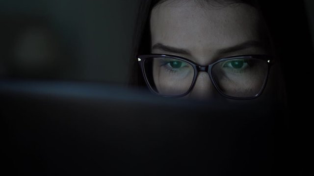 The girl in the shirt and glasses works behind the laptop. Close up face. 4k video