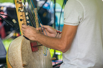closeup midsection of male artist in white t-shirt performing traditional wooden harp kora during event with focus on foreground