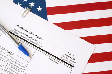 I-130 Petition for alien relative blank form lies on United States flag with blue pen from...