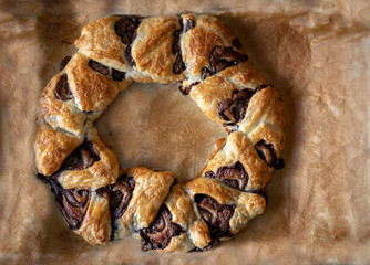 Chocolate puff pastry crown. Homemade sweet twists on a baking paper background.