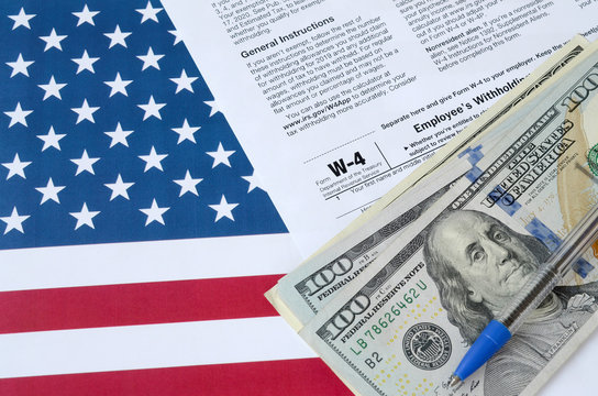 Form W-4 Employee's Withholding Allowance Certificate And Blue Pen With Dollar Bills Lies On United States Flag. Internal Revenue Service Tax Form