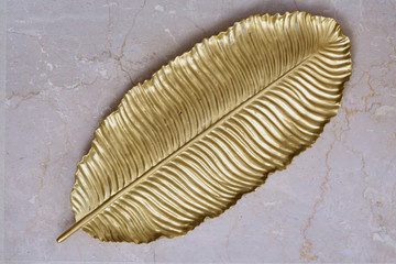Plate shape leaf, gold color on a marble table. flat lay