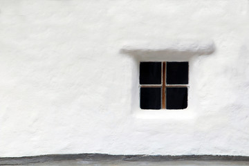 A wooden window of an old rural house built into a white concrete wall.
