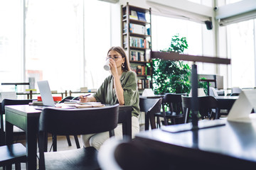 Young woman having drink while studying in library