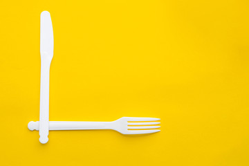 Plastic white fork and knife on yellow background. Cooking utensil. Top view. Minimalist Style. Copy, empty space for text
