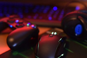 Modern gamepad and gaming mouse lies with keyboard and headphones on table in dark playroom scene....