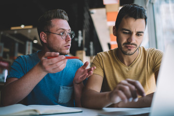 Confused male colleagues working on business project in cafe