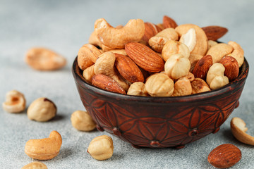 Healthy mix of different nuts in a bowl on a gray concrete or stone background. Almonds, hazelnuts,...