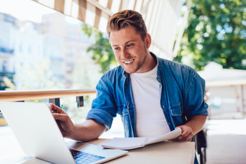 Content male freelancer in casual wear enjoying work with laptop at outdoors cafe veranda