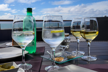 Drinking cold mineral water with bubbles, served in wine glass with ice cubes and lemon