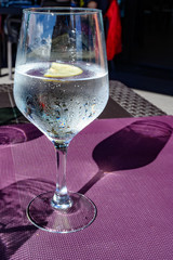 Drinking cold mineral water with bubbles, served in wine glass with ice cubes and lemon