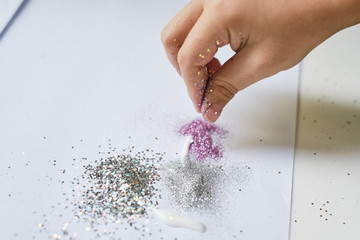 Kid's hand using fingers for pouring sparkles for create a picture