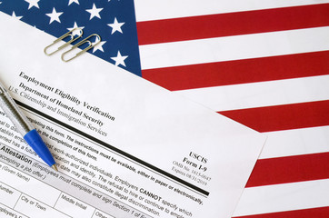 I-9 Employment Eligibility Verification blank form lies on United States flag with blue pen from...