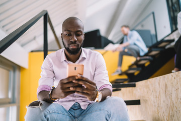 Serious young African American man using cellphone on stairs in college