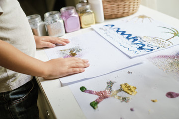 Child's hands and artworks made by child with glue and colourful glitter