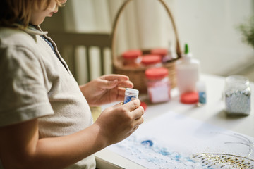 Child's hands opening the jar with blue glitter sparkles