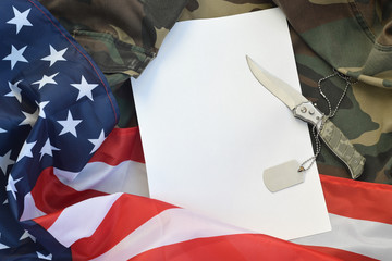 Blank paper lies with knife and army dog tag necklace on camouflage uniform and american flag
