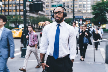 Thoughtful elegant male using wireless headphones on street