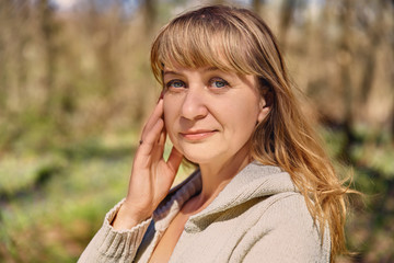 Portrait of beautiful long-haired woman. blonde enjoys nature, smiles pleasantly, touches cheek hand, thoughtfully thinks about aging retirement. Attractive mother with blue eyes looks sadly at camera