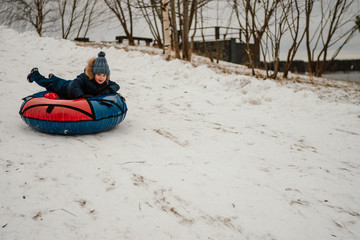 Fototapeta na wymiar adorable boy riding down the hill on the tubing bun in winter time