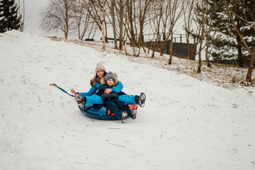 cute boy and his mother riding down the hill on inflatable snow tube in winter