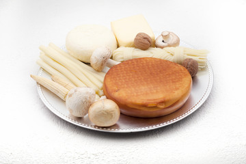 Fototapeta na wymiar Types of cheese, including smoked, hard, sour-milk and pigtail, on a silver plate, decorated with mushrooms, on a white background. The concept of cheese.
