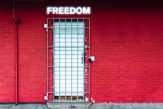 Red Wall with Door secured by Iron Gratings and the Word Freedom in Neon Letters
