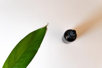 Top view of a bottle with CBD oil or any other essential oil and a green leaf on white background
