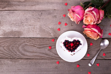 Mini romantic dessert cake for Valentine's Day with roses. Sweet cookies with cream topping and red heart for decor on wooden background. Close-up, copy space.