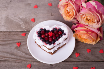Mini romantic dessert cake for Valentine's Day with roses. Sweet cookies with cream topping and red heart for decor on wooden background. 