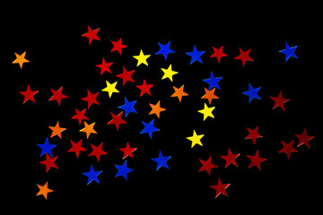 a scattering of blue, red, orange and yellow sequins in the shape of stars, isolate on a black background