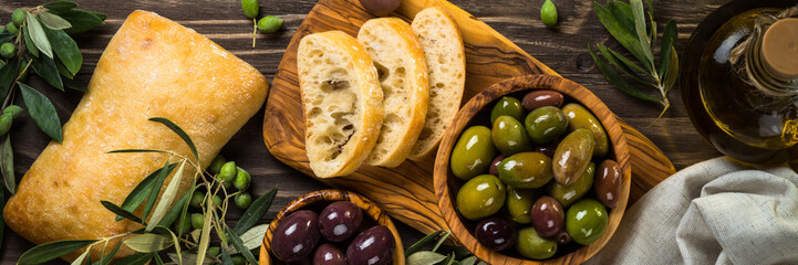 Olives, olive oil and ciabatta on wooden table.
