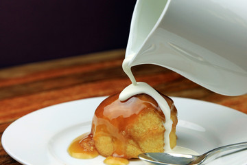 Fresh cream being poured over a treacle sponge pudding.