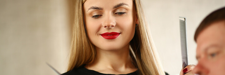 Woman Hairdresser Looking at Client Mobile Phone. Young Hairstylist Holding Comb and Scissors in Hands. Male Customer Showing Haircut to Stylist. Beautiful Stylist with Hairbrush in Beauty Salon