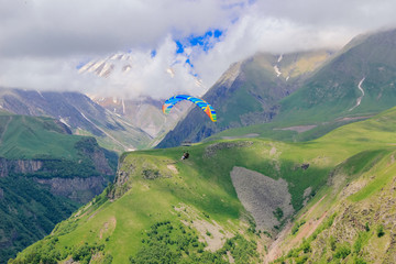 Two people on a paraglider fly in the green mountains