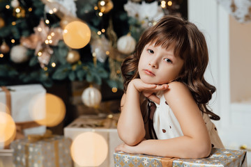 Holidays, childhood and people concept - smiling little girl with gift box over living room and christmas thee background. Luxurious Christmas decoration. Presents for Christmas and New Year. 