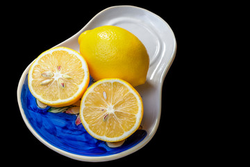 Whole lemon and two halves of lemon on a ceramic plate isolated on black background