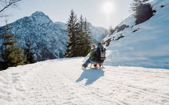 Speeding downhill on wooden sled. Happy influencers couple having fun with wood vintage sledding on snow high mountains - Young crazy people enoying winter vacation - Travel and holiday concept