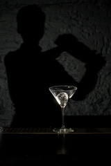 Bartender shadow holding a steel shaker on the bar counter with the bar equipment