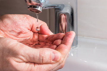 Water dripping from the faucet on the hands. Concept of saving water.