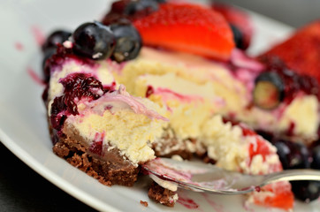 Close-up of half eaten strawberry, blueberry cheesecake on plate with spoon