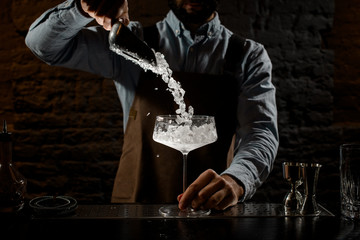 Male bartender putting a crushed ice to the big cocktail glass with special spoon