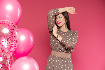 woman with perfect makeup and pink lipstick standing near air balloons with confetti and smiling. Concept celebrating, party, birthday