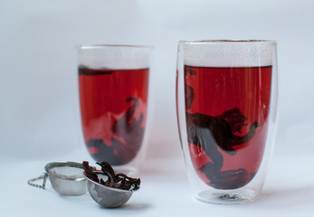 Two glass of hot hibiscus tea and strainer on white background.